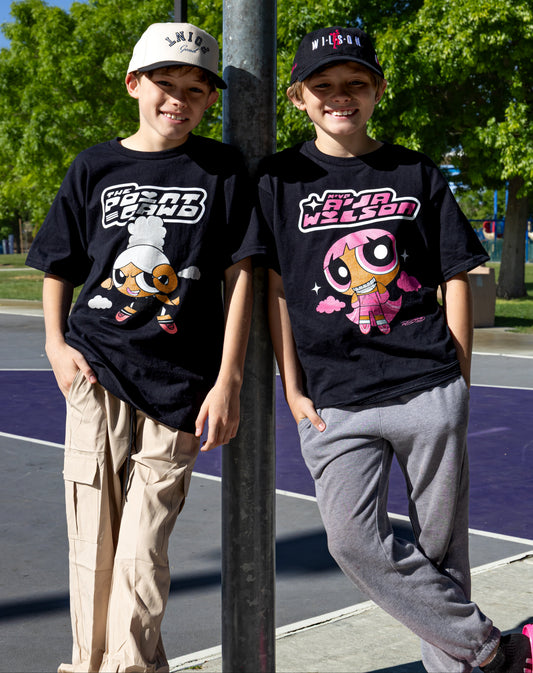 Two children wearing black t-shirts with cartoon characters on a street.